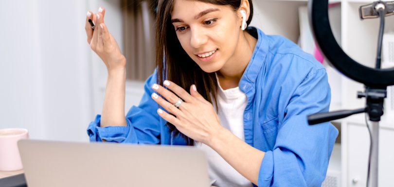 Girl blogger with earphones using laptop,chatting with followers in social network at home.