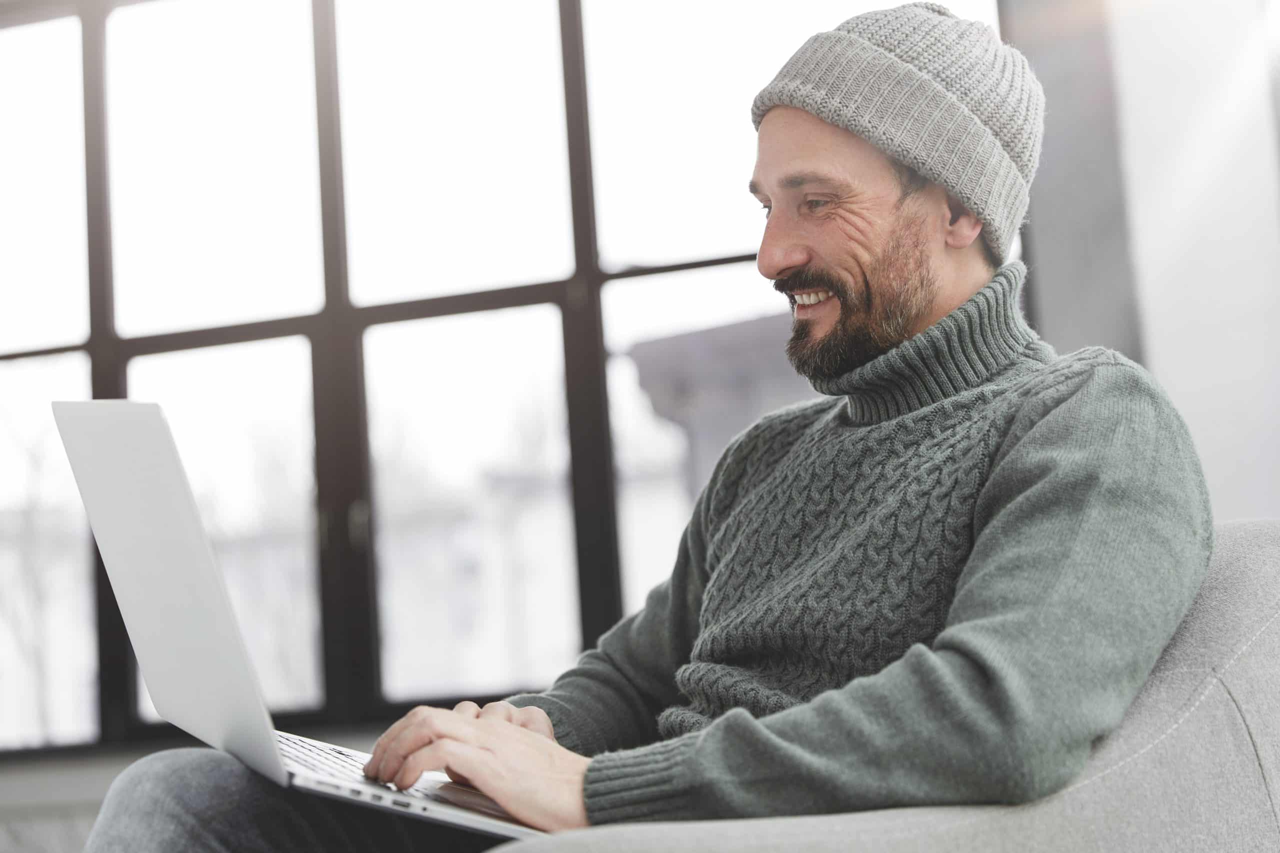Stylish unshaven male copywriter works remotely at modern computer device, has happy expression as recieves email from close person, connected to internet, surfes different websites. Technology